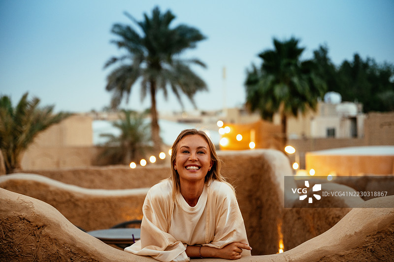 女性游客在美丽的中东屋顶咖啡馆里微笑着对着相机摆姿势，背景是日落。图片素材
