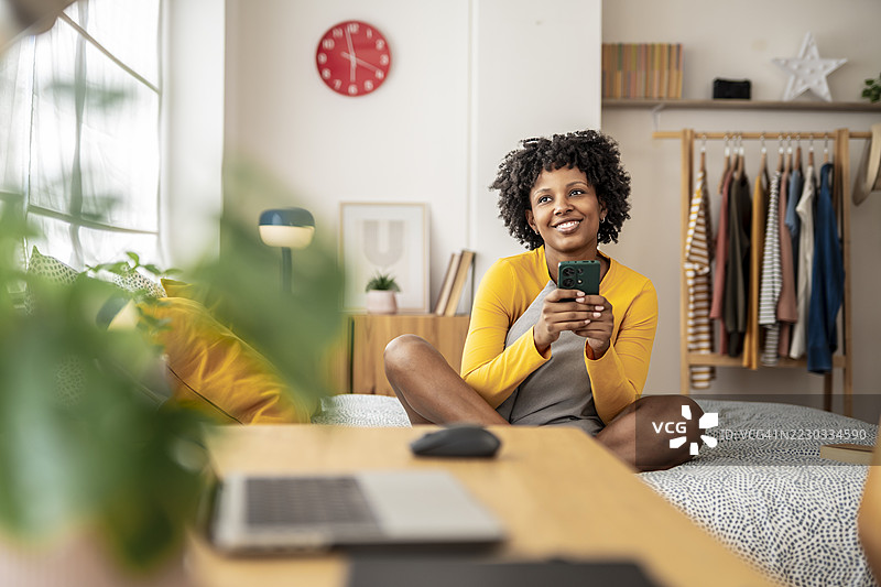 愉快的女性在温暖的卧室环境中，舒适地躺在柔软的床上，随意地浏览智能手机。图片素材