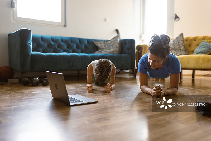母亲与孩子在家进行的健身锻炼，配有笔记本电脑指导图片素材