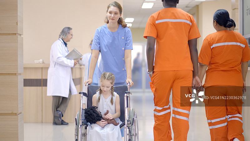 护士带着一个面带灿烂笑容的小女孩走进医生的检查室，其他患者和家属则在候诊区等候。医院环境突显了医疗中关怀和同情的重要性。图片素材
