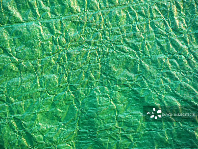 皱褶的绿色塑料篷布特写。粗糙的纹理。阳光。自然色彩和风化效果。法国,上萨瓦省,埃维昂-莱-班。图片素材