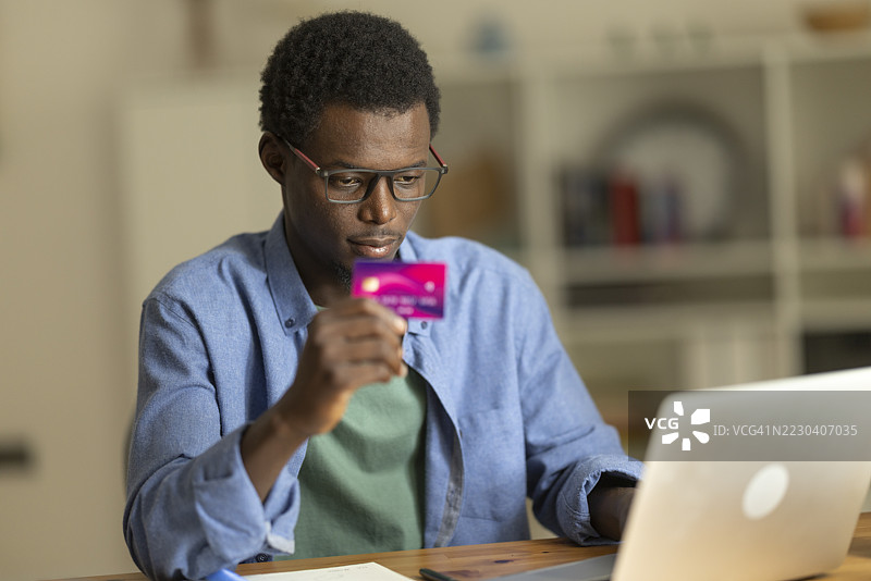 年轻男子专注于在笔记本电脑上输入信用卡信息进行在线交易图片素材