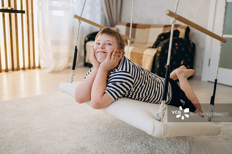 快乐的唐氏综合症儿童在家里的秋千上放松。图片素材