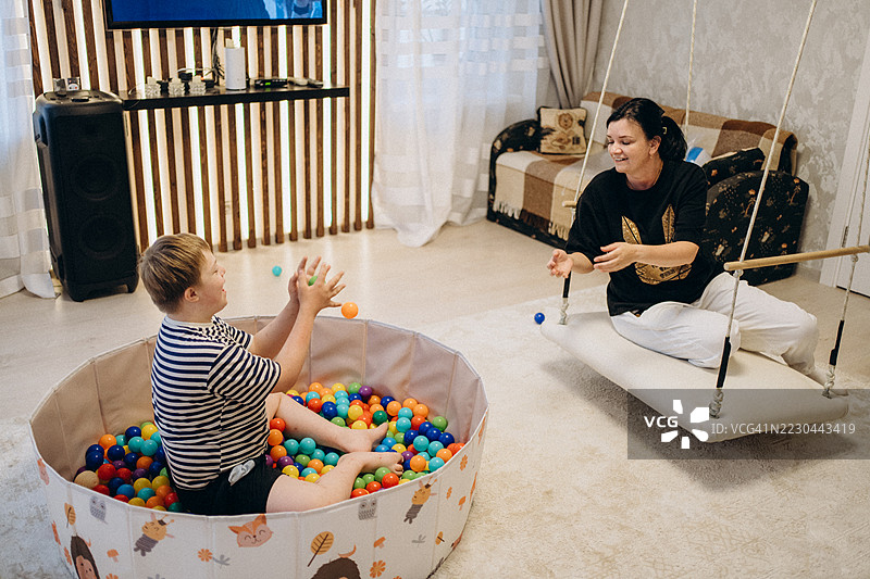 唐氏综合症儿童与治疗师在秋千上玩五彩斑斓的球。图片素材