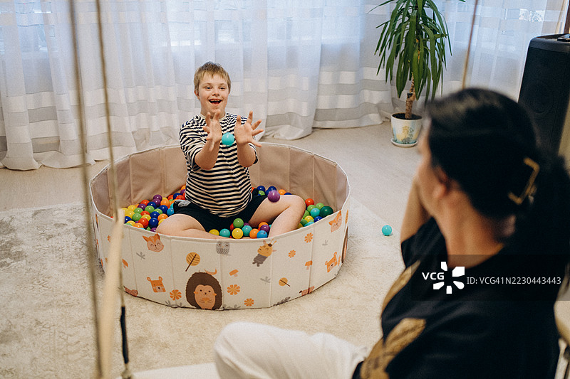 快乐的唐氏综合症儿童在家中玩五彩斑斓的球。图片素材