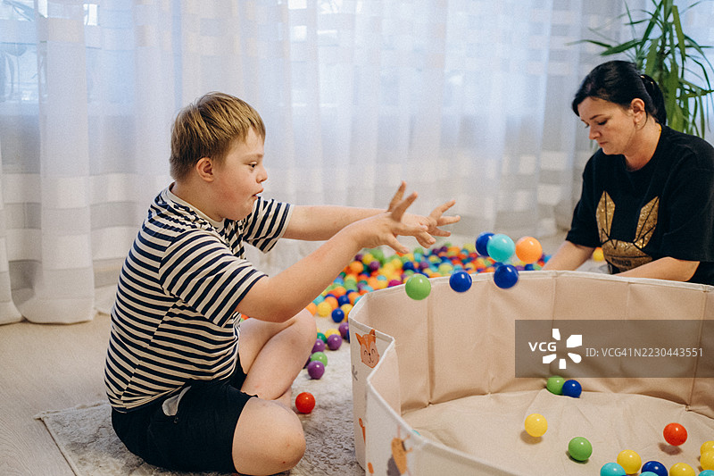 患有唐氏综合症的孩子与他的母亲一起玩五彩斑斓的球。图片素材