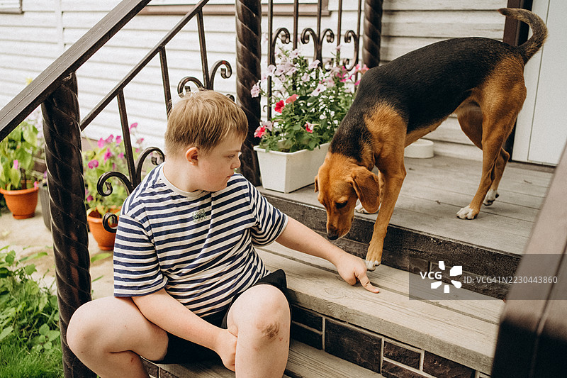 唐氏综合症儿童在门廊台阶上与狗玩耍图片素材