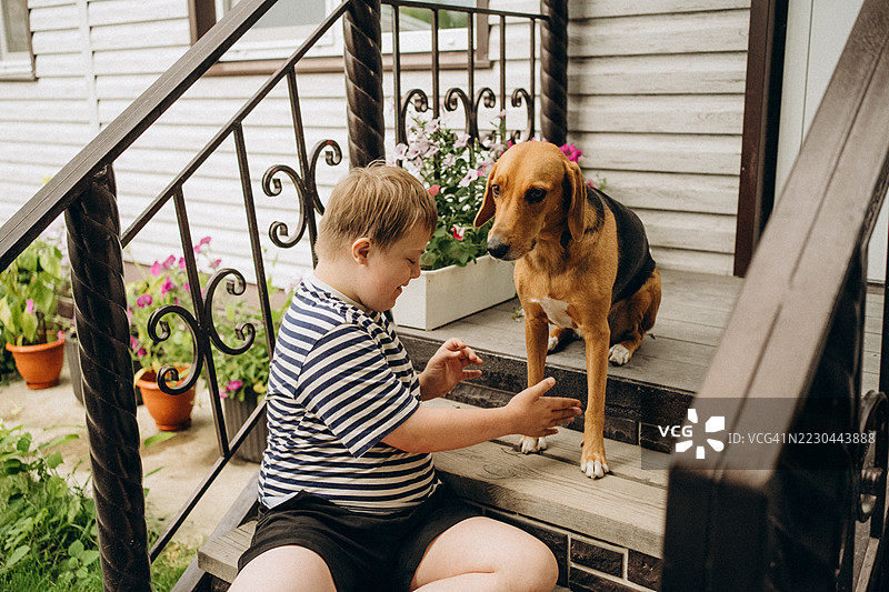 快乐的唐氏综合症儿童在门廊台阶上与狗玩耍图片素材