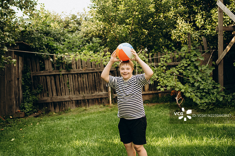 快乐的唐氏综合症儿童在花园里玩球图片素材