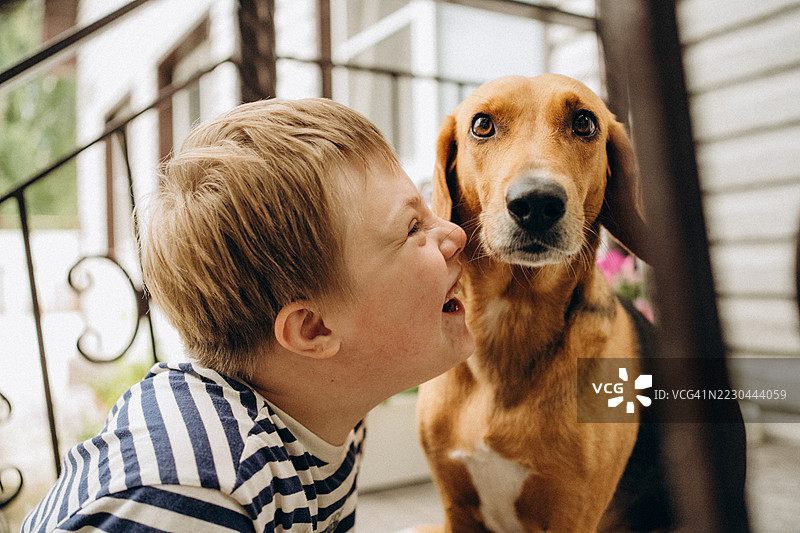 金发的唐氏综合症儿童在门廊上与狗玩耍图片素材