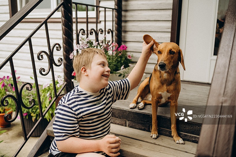 快乐的唐氏综合症儿童在门廊台阶上与狗玩耍图片素材