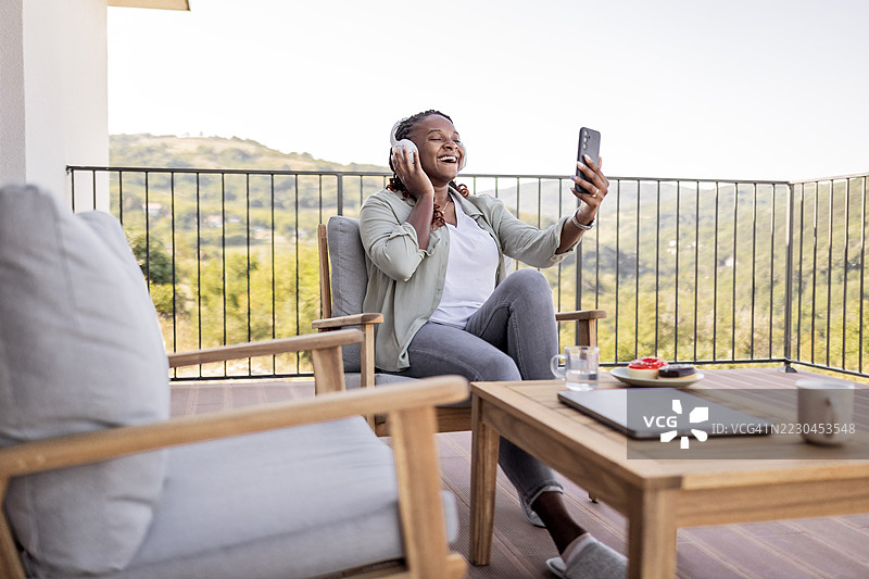 非裔美国女性在阳台上使用智能手机，戴着耳机进行视频通话图片素材