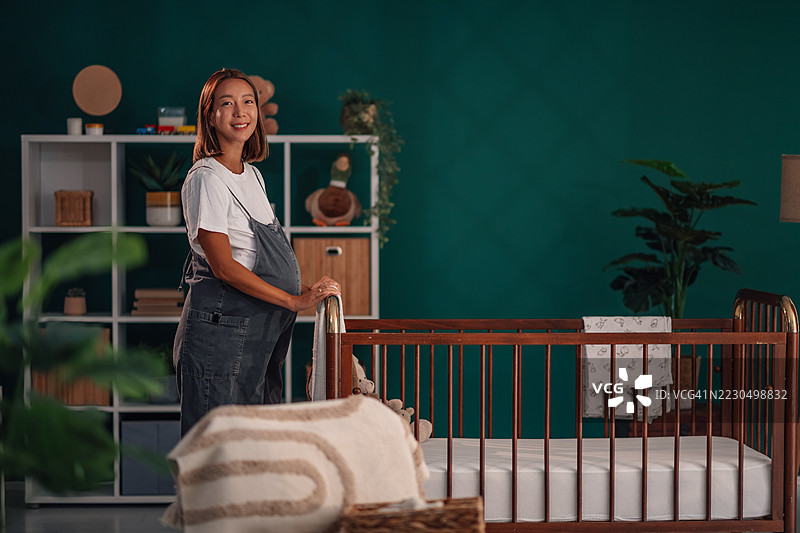 准妈妈微笑着站在婴儿床旁，为宝宝的到来做好准备图片素材