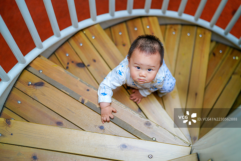 爬行的亚洲宝宝抬头看向镜头，正在爬上台阶，一岁大图片素材