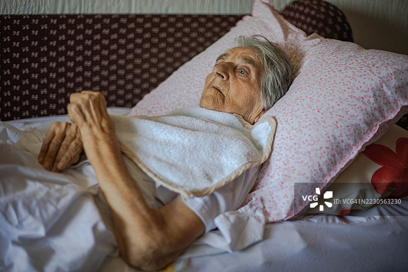 一位神志不清的老妇人躺在床上，目光呆滞。图片素材