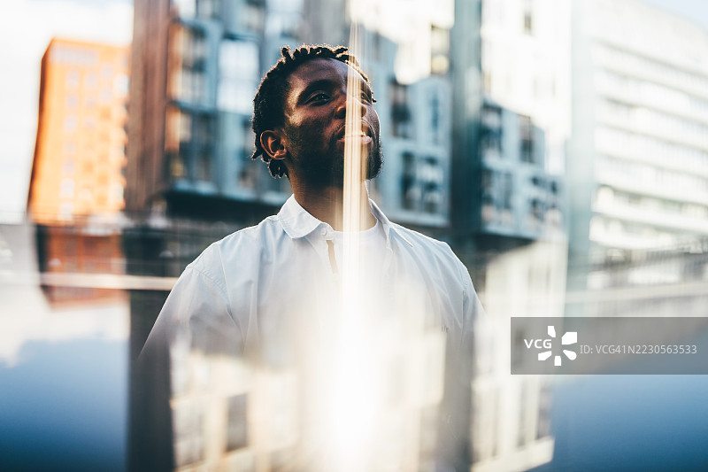 一名穿着白衬衫的男子站在城市景观前，光线反射营造出超现实的效果。图片素材