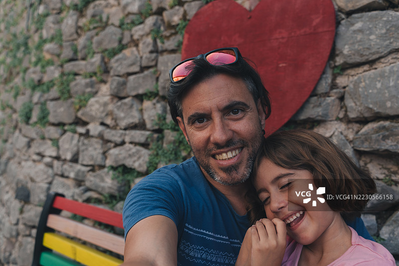 父亲和女儿在彩虹长椅上微笑着看向镜头图片素材