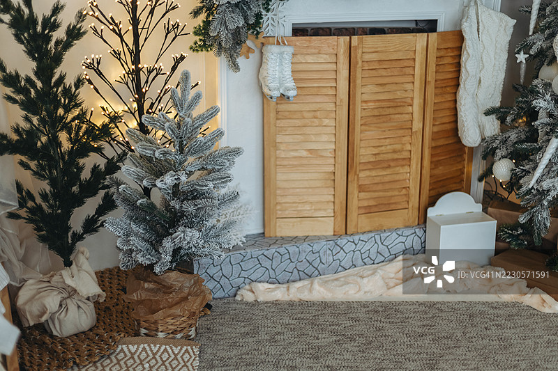 装饰华丽的圣诞树靠近一个有纹理的壁炉台，壁炉旁装饰着木质百叶窗和悬挂的白色圣诞袜。图片素材