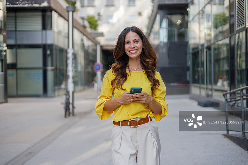 职业女性在城市景观中穿行，微笑着在午间通勤时查看智能手机图片素材