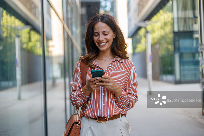 职业女性在城市街道上行走，手持智能手机，进行网络交流和数字沟通。图片素材