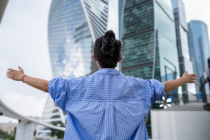 在现代城市景观中张开双臂的女商人，象征着成功与自由图片素材