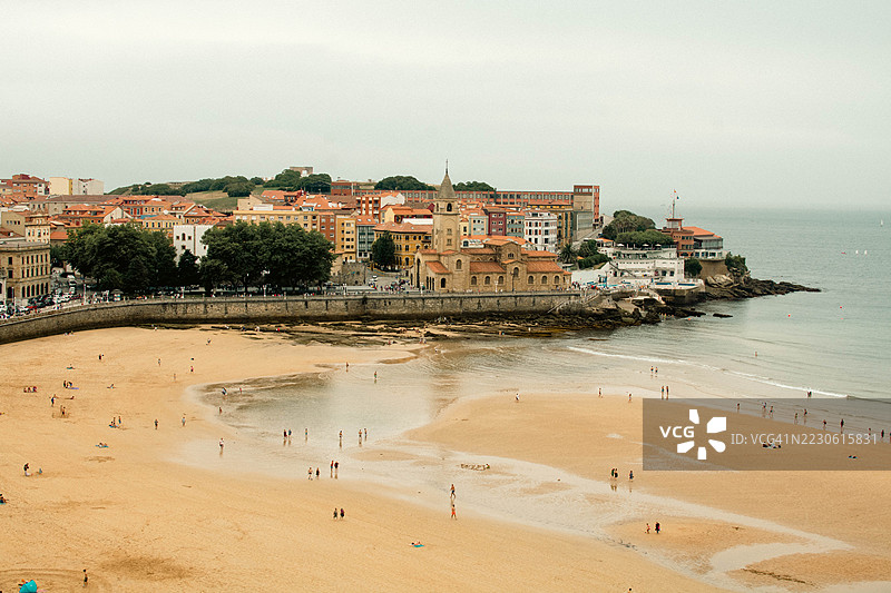 游客在西班牙希洪海滩放松，背景是色彩缤纷的建筑和教堂图片素材