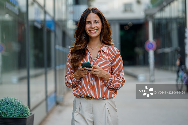 自信的职业女性在城市环境中大步前行，手握智能手机，散发着成功与积极的气息图片素材
