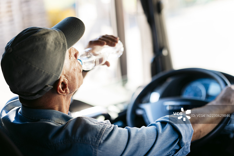 资深卡车司机在阳光明媚的日子里开车时喝水图片素材