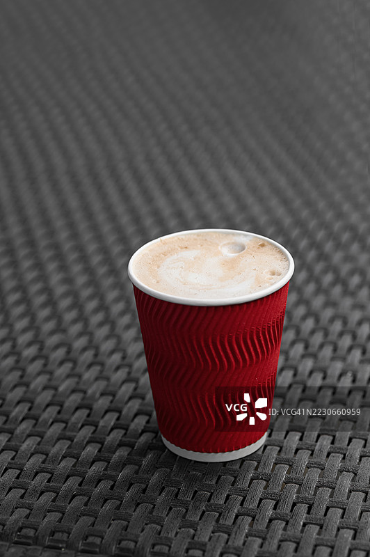 红色一次性咖啡杯，泡沫在藤编户外桌上图片素材