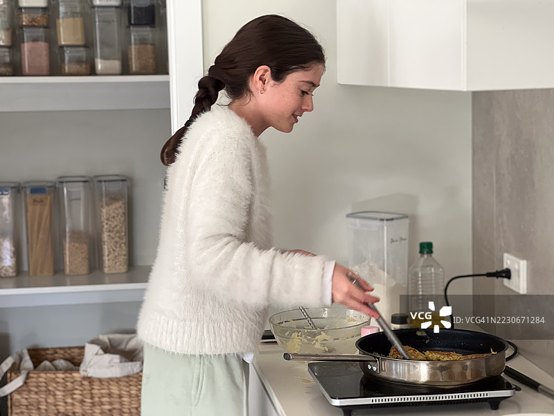 年轻女孩在家里的电炉上用煎锅煮鸡蛋图片素材