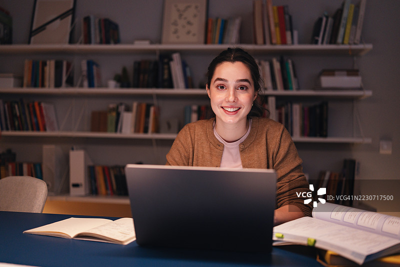 微笑的女学生在舒适的图书馆环境中使用笔记本电脑学习图片素材
