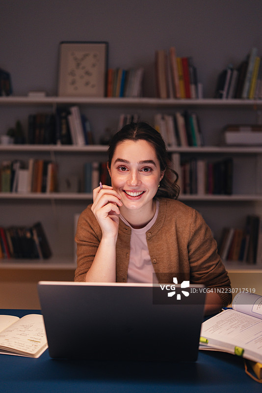 年轻学生在家里的图书馆里夜晚用笔记本电脑学习图片素材