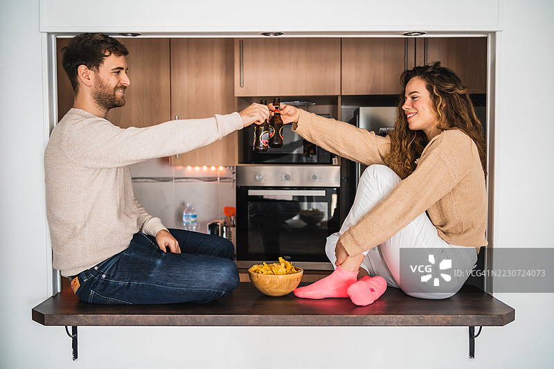 年轻情侣在厨房台面上举杯庆祝，手中拿着啤酒瓶图片素材