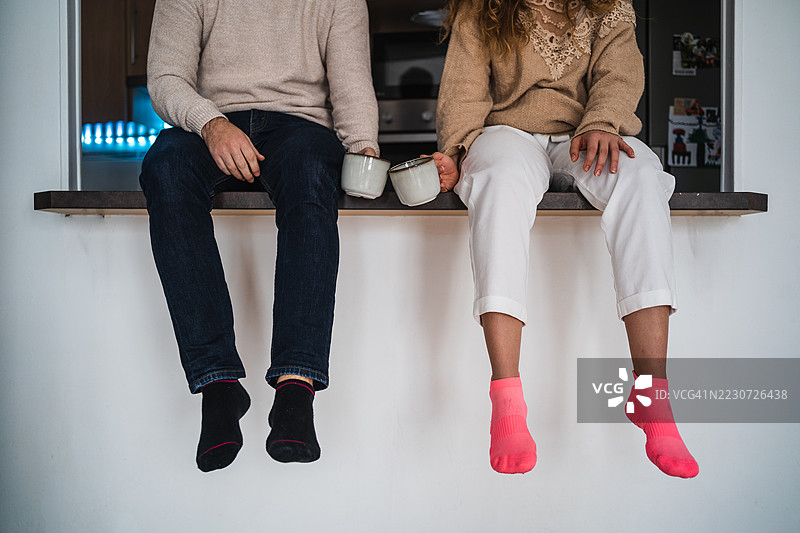 一对情侣穿着彩色袜子坐在厨房台面上喝咖啡图片素材