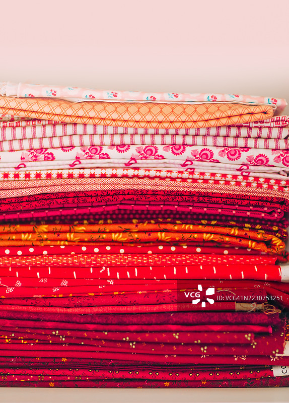 一堆红色和橙色图案的织物。五颜六色的折叠红色、橙色和图案纺织品整齐地堆放，适合缝纫或手工艺。图片素材