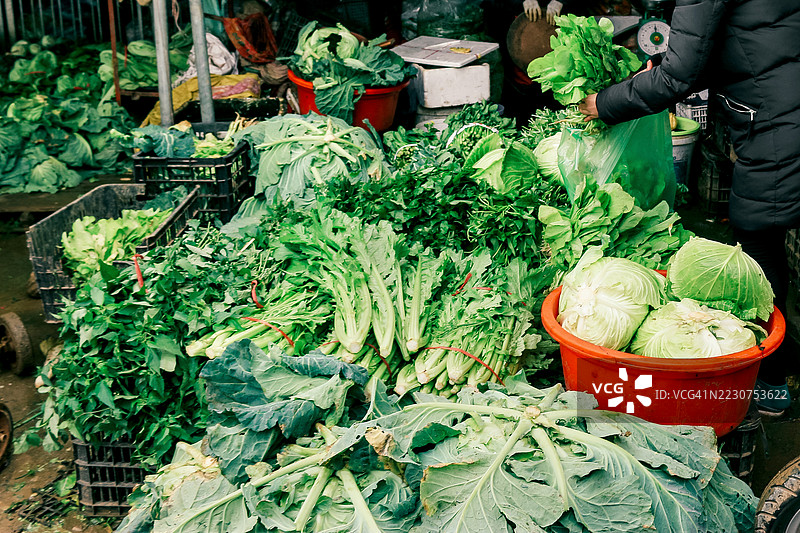 女性在市场摊位购买芥菜叶蔬菜图片素材