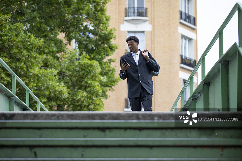 穿着得体的年轻男子在天桥上提着包，使用智能手机。图片素材