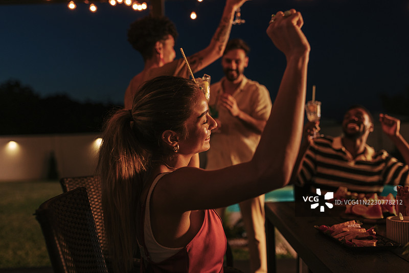 朋友们在花园的游泳池旁举起手来，享受夏夜派对图片素材