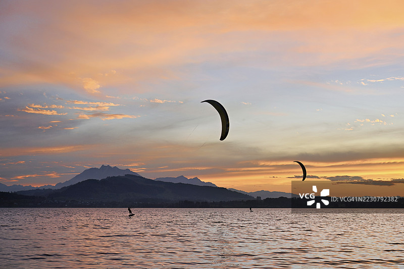 日落时分，两名风筝冲浪者在楚格湖上，背景是皮拉图斯山，瑞士楚格州。图片素材