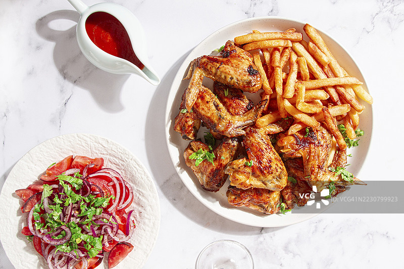 美味的烧烤鸡翅，配有薯条、沙拉和清爽的饮料，摆放在一个舒适的桌子上，没有人。图片素材
