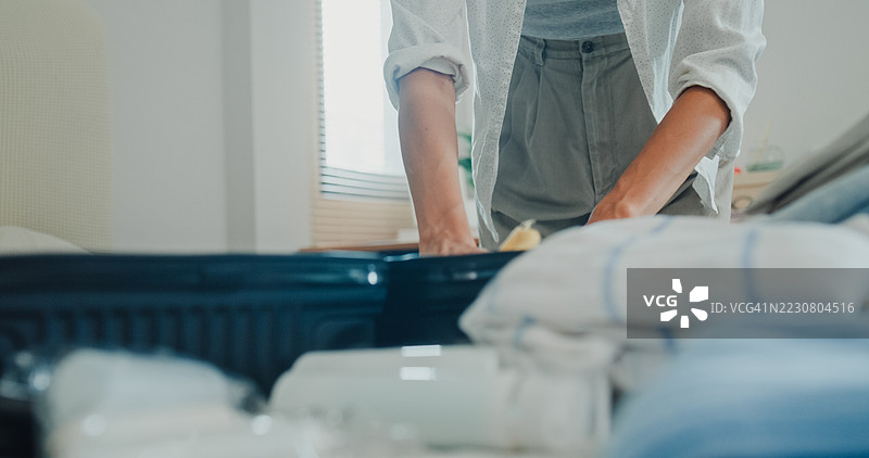 年轻的亚洲女性在卧室的床上打包行李，准备衣物和个人物品，为一个轻松的夏季假期旅行做准备。图片素材