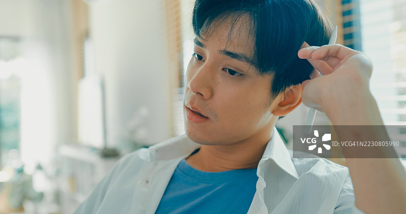 年轻亚洲男性在家工作，近距离观察他在电脑屏幕上分析财务数据，反映出现代家庭办公室的布置和远程工作的场景。远程工作与财务。图片素材