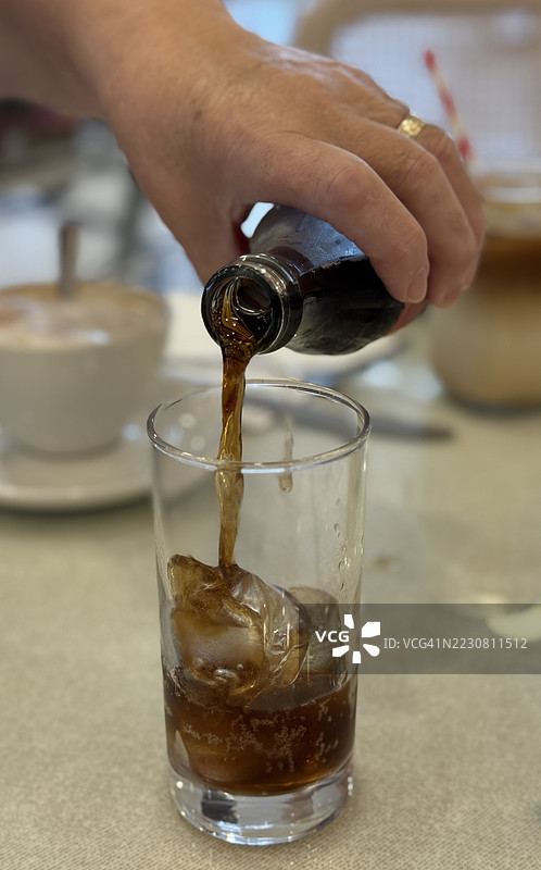 特写镜头下，桌子上有人将饮料倒入装有冰块的玻璃杯中。图片素材