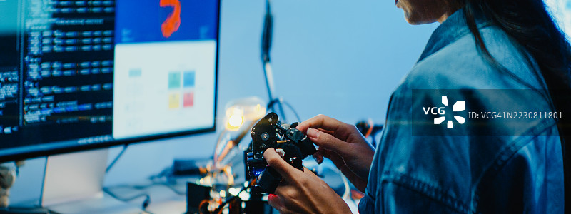 年轻女性工程师在夜间的科技实验室里加班，专注于机器人手臂原型的工作。机器学习、计算机制造、创新与创造力。人工智能与机器人开发。图片素材