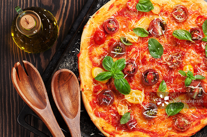 新鲜出炉的披萨，上面有番茄、马苏里拉奶酪和罗勒，摆放在木桌上图片素材