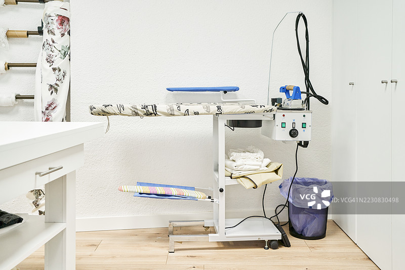 专业熨烫站，配有折叠的衣物和面料，位于裁缝工作室内图片素材