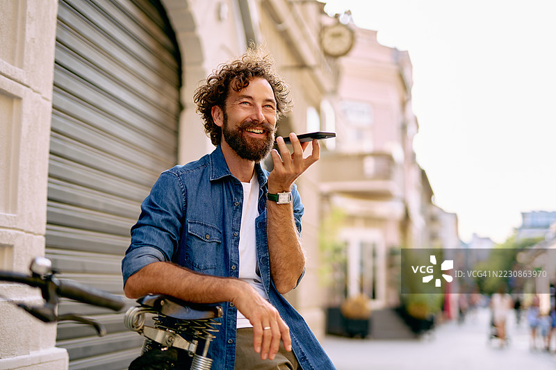时尚男士坐在自行车上通过手机发送语音信息图片素材