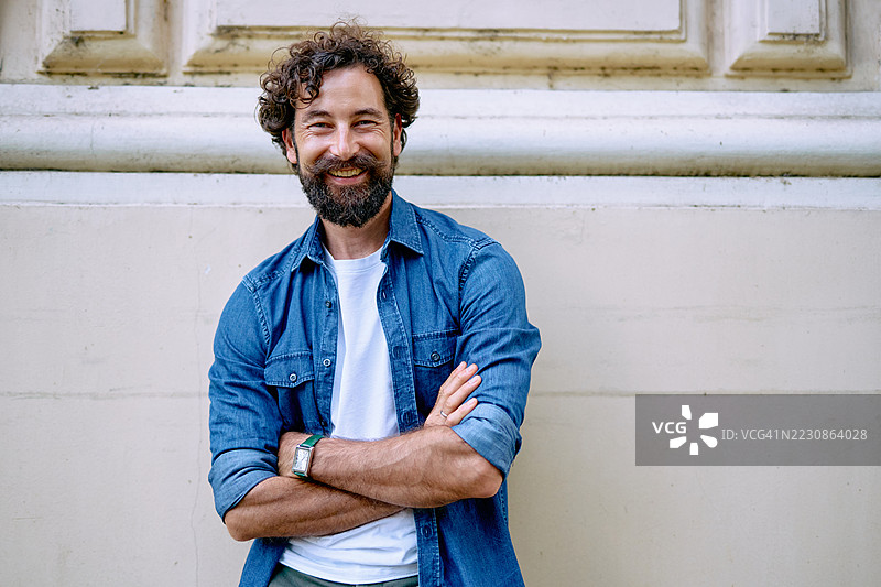 微笑的男子交叉双臂站在墙边图片素材