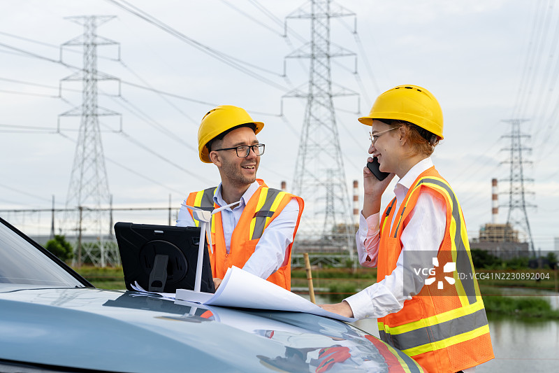 工程师在电力线附近讨论计划并使用平板电脑图片素材