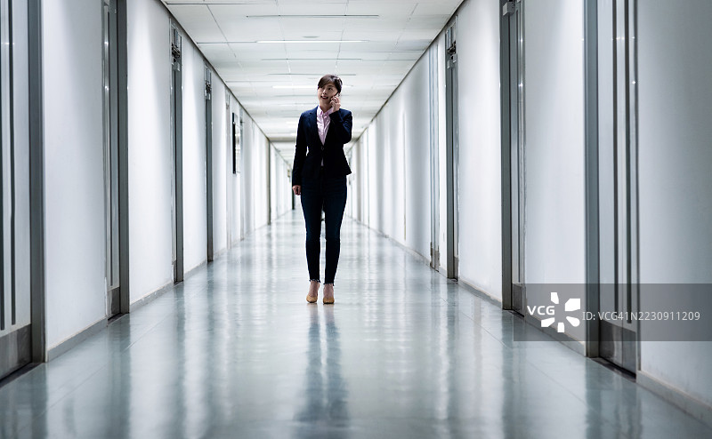 走廊中走动并使用手机的女性图片素材